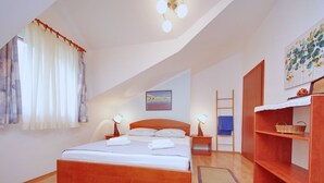 A bedroom with a wooden bed, two bedside tables with lamps, a wooden wardrobe, a painting on the wall, and a window with curtains. - Seafront Apartments Deveron - Duplex Two Bedroom Apartment with Balcony and Sea View (Jelsa)