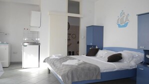 Une chambre à coucher avec un lit, une armoire, un bureau et une salle de bain visible à travers une porte ouverte.