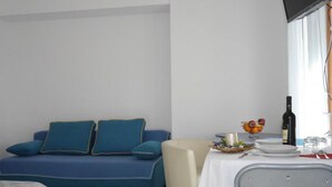 Une pièce avec un canapé bleu, une petite table recouverte d’une nappe blanche et une chaise.