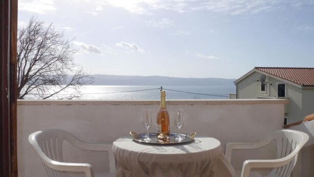 Un balcon avec une table dressée pour deux personnes, offrant une vue sur une étendue d’eau et une côte lointaine.