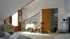 Une chambre d’hôtel avec un lit, une table à manger avec des chaises, un téléviseur et une salle de bain visible à travers une porte ouverte.