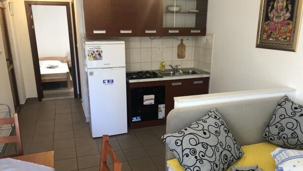 Cocina compacta con refrigerador, estufa y lavamanos. Cuenta con una pequeña zona de comedor con una silla y una mesa.