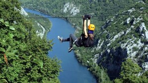 Una persona haciendo bungee jumping con un río y montañas al fondo.