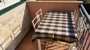 A small outdoor patio with a checkered table and chairs, a stone wall, and a metal railing.