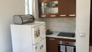 A compact kitchen with a built-in oven, a toaster, and a window with a curtain.