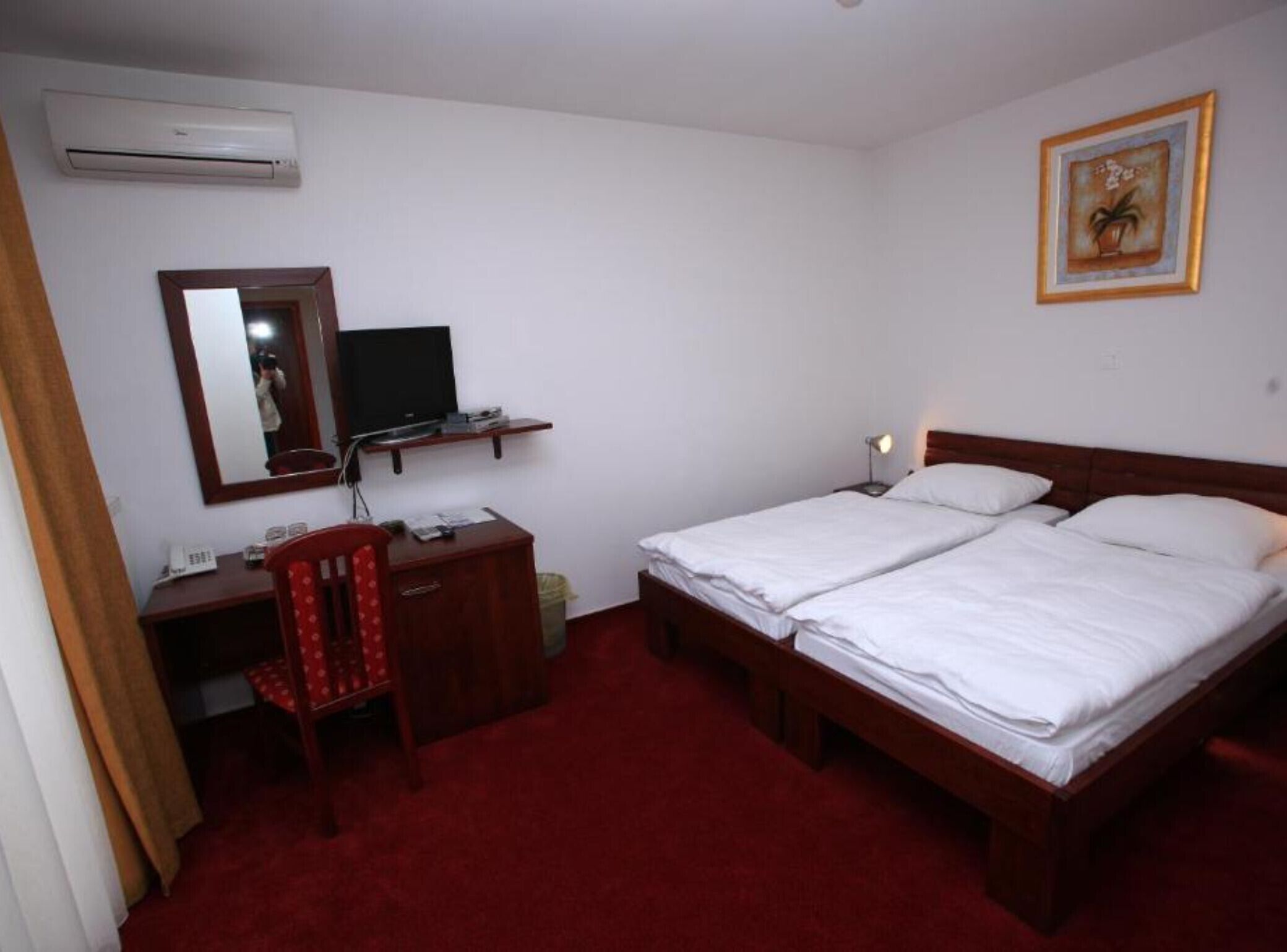Quarto de hotel com escrivaninha, cadeira, duas camas, televisão e um quadro na parede.