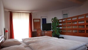 Una camera d'albergo con un letto, una scrivania, una televisione e una pianta in vaso.