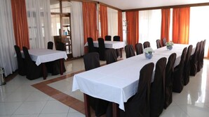 A conference room with multiple tables and chairs, large windows with orange curtains, and a tiled floor. - Hotel Orion - Single Room with Balcony (Ivanec)