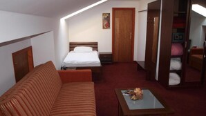 A hotel room with a bed, a sofa, a table, a wardrobe, and a painting on the wall. - Hotel Orion - Single Room with Mountain View (Ivanec)