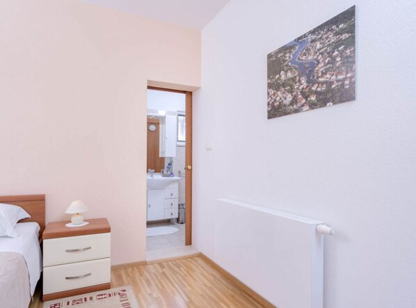A bedroom with a bed, bedside table, and a nightstand. There is a door leading to a bathroom with a sink and mirror.