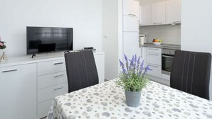 A modern, compact living space with a dining area, kitchenette, and a flat-screen TV.