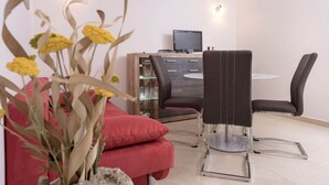 A modern dining area with a round table, two chairs, a red sofa, and a wooden cabinet with a television. - One Bedroom Apartment with Terrace (Vrboska)