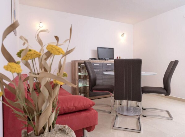 A modern dining area with a round table, two chairs, a red sofa, and a wooden cabinet with a television.