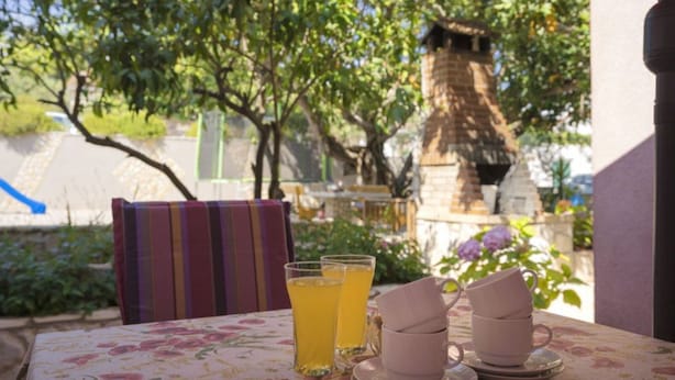 A table with a floral tablecloth, two glasses of yellow beverage, and three stacked cups. - One Bedroom Apartment with Terrace (Vrboska)