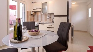 A modern kitchen with white cabinets, a built-in oven, and a microwave. There is a dining area with a round table and two chairs. - One Bedroom Apartment with Terrace (Vrboska)