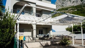 A modern multi-story building with balconies, a covered outdoor area, and a mountain backdrop.