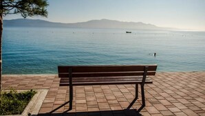 A bench on a paved walkway overlooking a calm body of water with distant mountains.