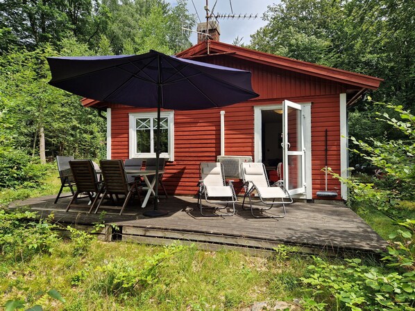 A red wooden cabin with a deck, outdoor seating, and a large umbrella.
