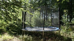 Ein Trampolin, umgeben von einem Maschengitter, in einem bewaldeten Gebiet.