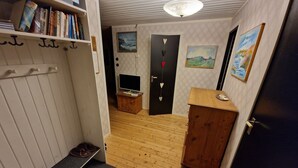 Ein schmaler Korridor mit Holzboden, einer kleinen Kommode, einem Fernseher auf einem Standfuß und einer Tür mit Herzverzierung.