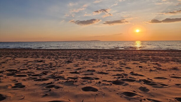 Ein Strand mit Fußabdrücken und einem Sonnenuntergang über dem Wasser.