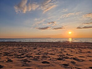 A beach with footprints and a sunset over the water.
