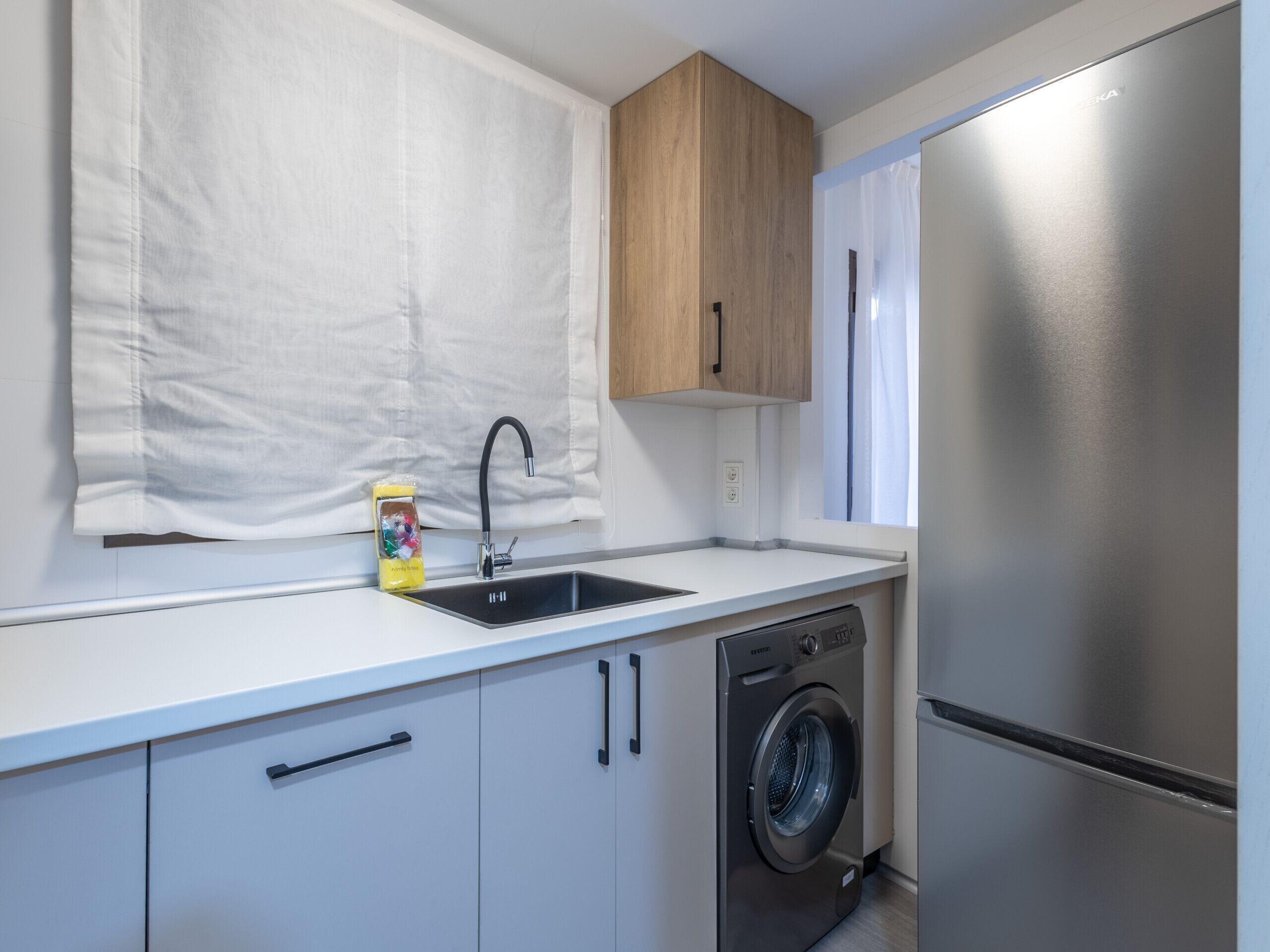 Une cuisine moderne équipée d’un réfrigérateur en acier inoxydable, d’un lave-linge et d’un évier surmonté d’un meuble en bois.