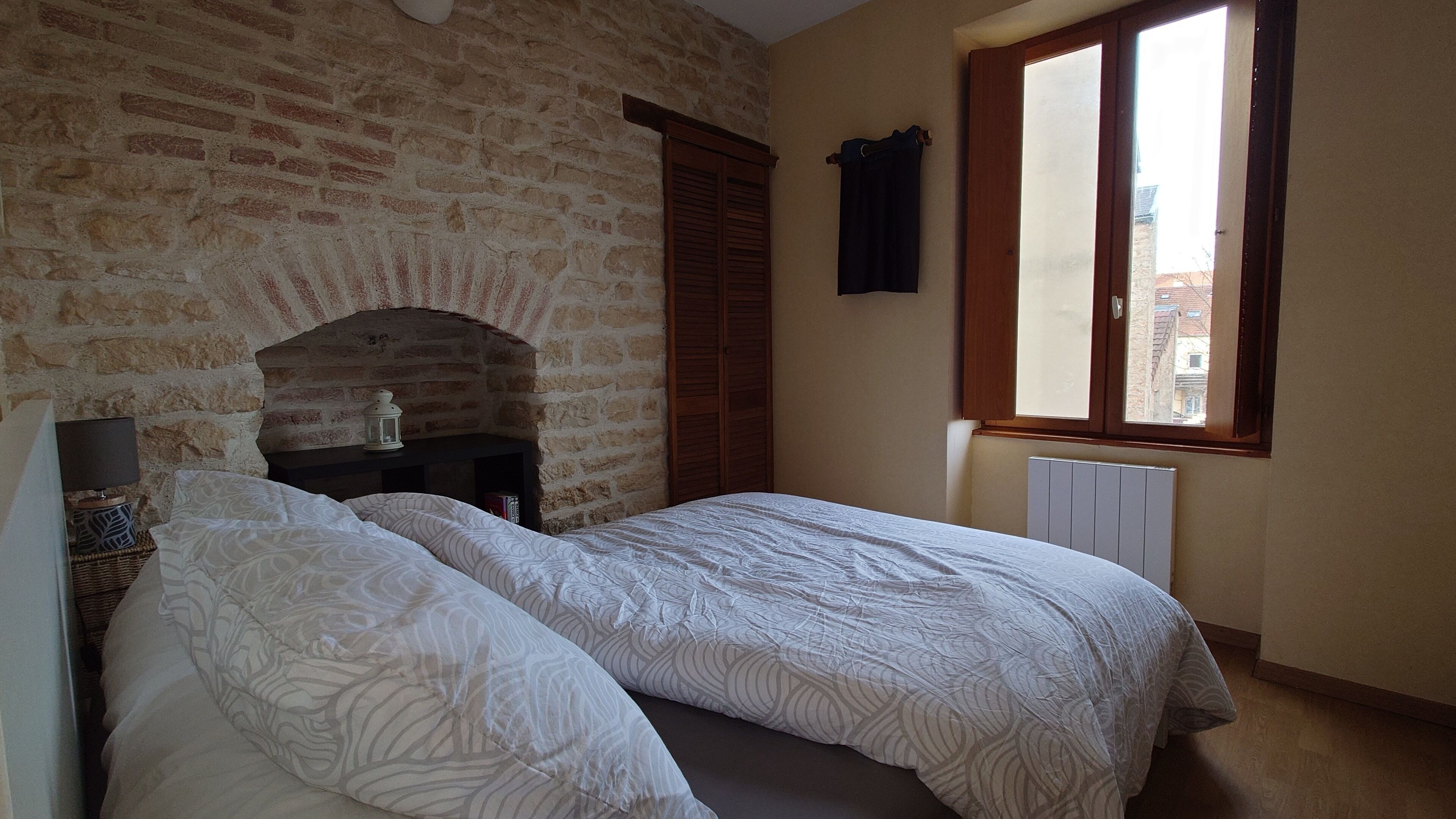 Een slaapkamer met een bakstenen muur, een houten garderobe, een raam met uitzicht en een radiator.