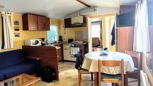 A compact living space with a kitchenette, a dining area, and a sofa. - FULLY EQUIPPED MOBIL HOME with large 30 M2 terrace and small garden. (Saint-Augustin)
