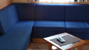 A living area with a blue sofa, a wooden coffee table, and a window with curtains. - FULLY EQUIPPED MOBIL HOME with large 30 M2 terrace and small garden. (Saint-Augustin)