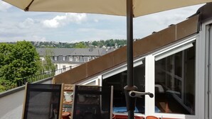 A balcony with a beige umbrella, potted plants, and a view of a cityscape. - Duplex apartment over 2 levels with roof terrace near the Elbe in Dresden-Blasewitz (Dresden)