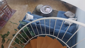 A living room with a blue sofa, a coffee table, and a staircase. - Duplex apartment over 2 levels with roof terrace near the Elbe in Dresden-Blasewitz (Dresden)