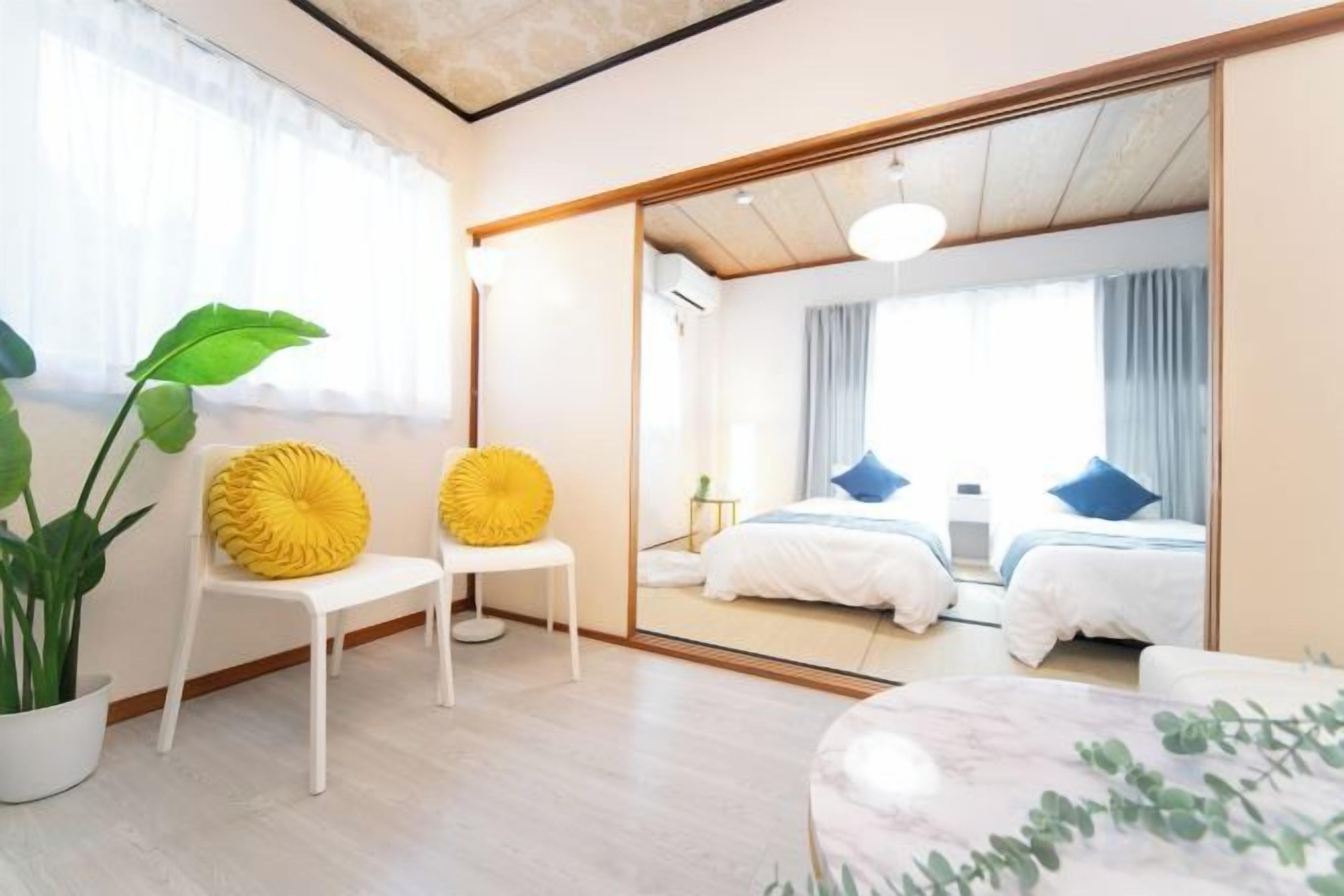 A modern hotel room with a large mirror, two beds, a seating area with chairs, and a potted plant.