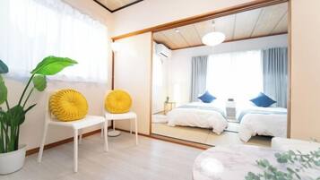 A modern hotel room with a large mirror, two beds, a seating area with chairs, and a potted plant.