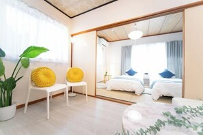 A modern hotel room with a large mirror, two beds, a seating area with chairs, and a potted plant. - Suzuka Smile Room (Suzuka)