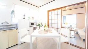 A modern kitchen with white cabinets, a dining table, and a sliding glass door leading to a living area. - Suzuka Smile Room (Suzuka)