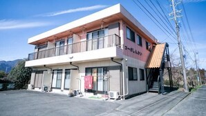 A two-story building with a balcony on the upper floor, a visible entrance, and a small outdoor area with a red towel hanging. - Suzuka Smile Room (Suzuka)
