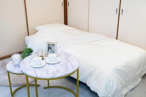 Una cama bien hecha con ropa blanca, una mesita redonda con mantel blanco y un marco de fotos sobre la cama.
