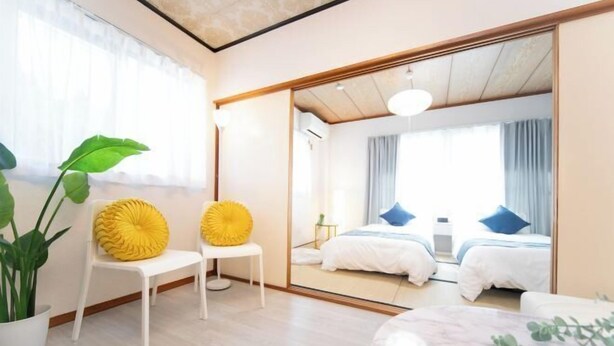 A modern hotel room with a large mirror reflecting the bed and curtains, a potted plant, and a small table. - Suzuka Smile Room (Suzuka)