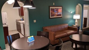 A room with a brown leather sofa, a round dining table, and a kitchen area visible through an archway. - WorldMark Spencer Street - 1 Bedroom (Las Vegas)