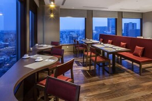 A restaurant with high tables and booths, large windows, and a city view.