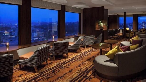 Ein moderner Lounge-Bereich mit großem Fenster und Blick auf die Stadt, bequemen Sitzmöglichkeiten und einem gemusterten Teppich.