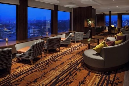 A modern lounge area with a large window offering a city view, plush seating, and a patterned carpet.