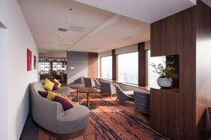 Un moderno vestíbulo de hotel con zonas de estar, una escalera y ventanas amplias.
