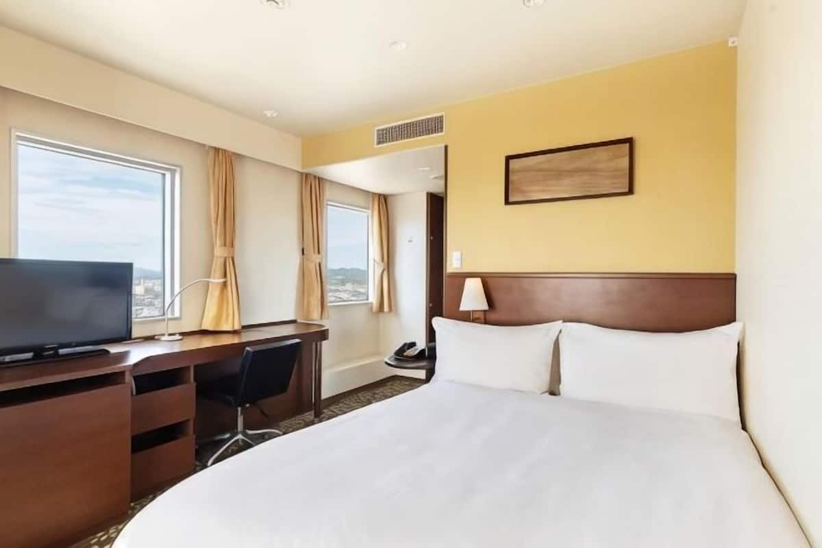 A hotel room with a bed, a desk, a television, and a city view.