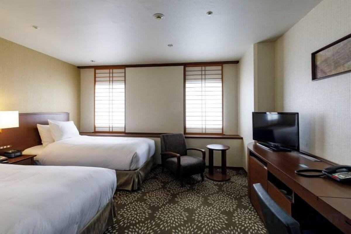 Une chambre d’hôtel avec deux lits, un bureau, une chaise, une télévision et une petite table.