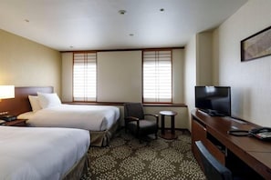 A hotel room with two beds, a desk, a chair, a television, and a small table.
