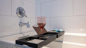 A bathtub with a glass tray holding a glass of wine, a shampoo bottle, and a blue and white spherical object. - **Cleaning Fee Included** Mini modern cabin nestled in the peaceful hills between Jackson and Putnam County, minutes away from CUMMINS FALLS STATE PARK. Designed for comfort and style, this vacation rental seamlessly blends modern charm with wooded s (Cookeville)