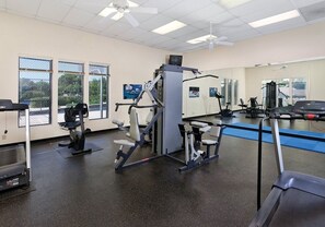 A gym with exercise equipment, large windows, and a mirrored wall.