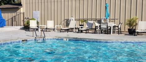Una piscina con sillones de descanso y un edificio grande al fondo.